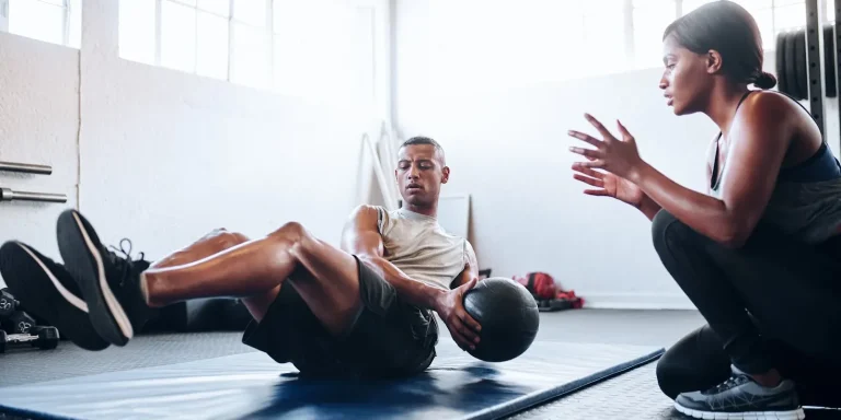 personal trainer with client doing weighted ball twist